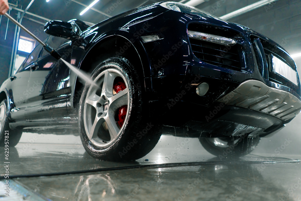 Close-up of a male car wash employee washing the rim and tire of a black luxury car using a high-pressure washer 