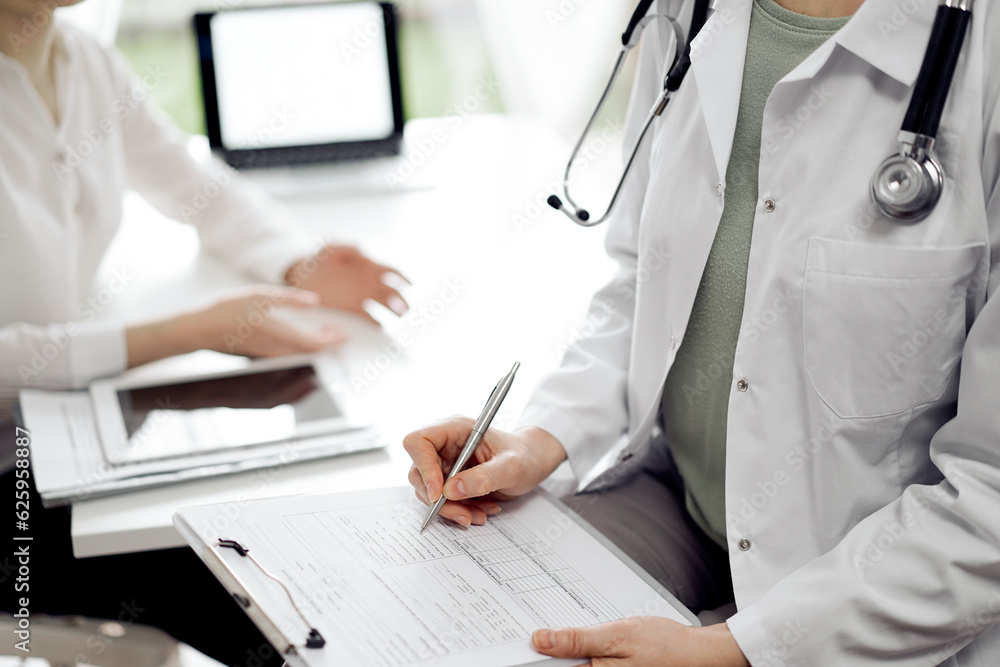 Doctor and patient view. Female physician is filling up a records from opposite a woman having a medical examination. Medicine concept Doctor and patient view. Female physician is filling up a records from opposite a woman having a medical examination. Medicine concept