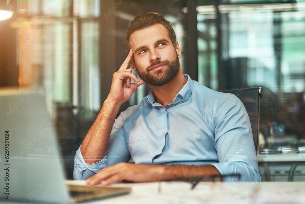 Thinking about business. Young bearded man in formal wear touching his head, smiling and looking away while working in modern office Thinking about business. Young bearded man in formal wear touching his head, smiling and looking away while working in modern office