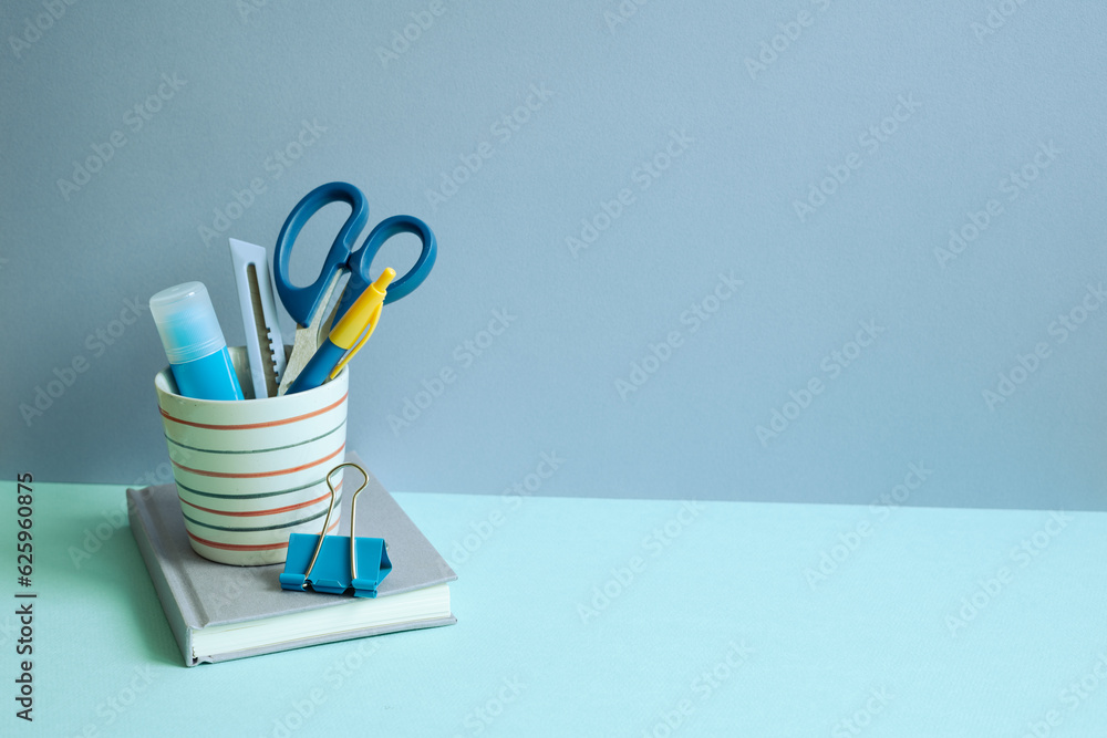 Writing supplies in pen holder and notebook on blue desk. blue wall background. workspace