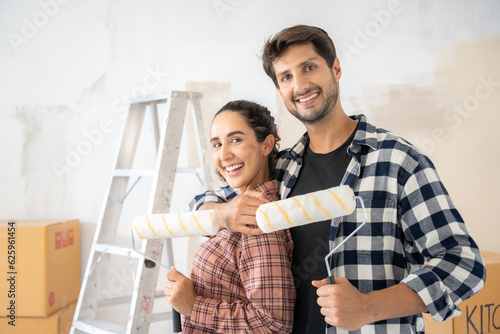 Εκτύπωση καμβά Happy Brazilian couple holding roller in hand and looking to camera at new home location