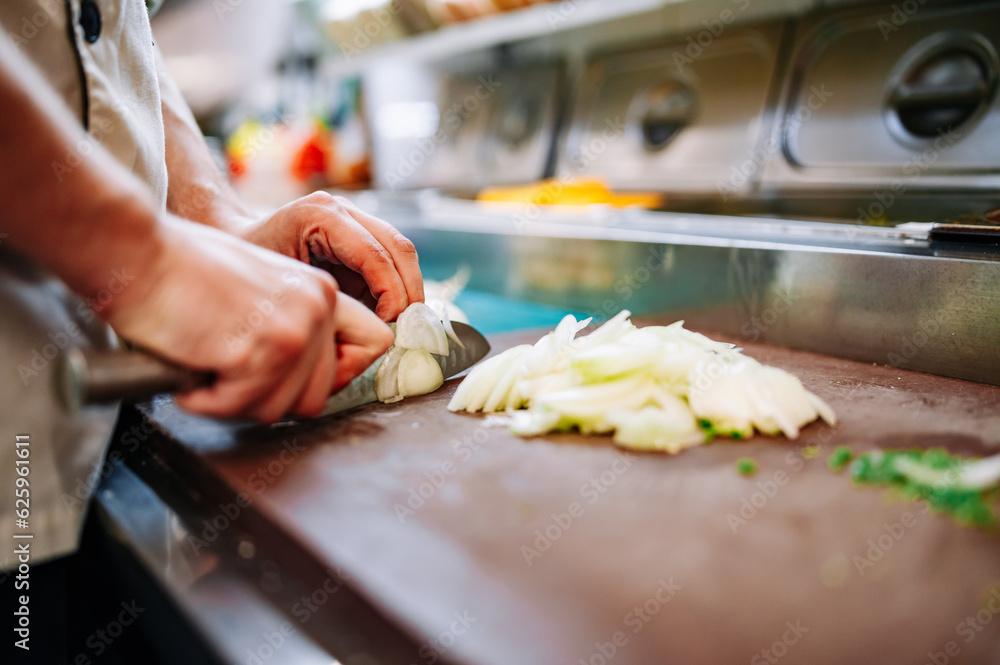 Chefs man hands chopping onion on wooden board in kitchen