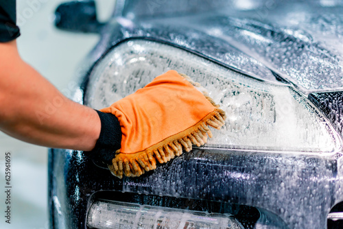 Close-up of a car wash worker using a microfiber cloth to wash a black luxury car with car wash shampoo