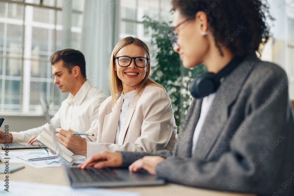 Smiling woman manager working on laptop in modern coworking while sitting near colleagues Smiling woman manager working on laptop in modern coworking while sitting near colleagues