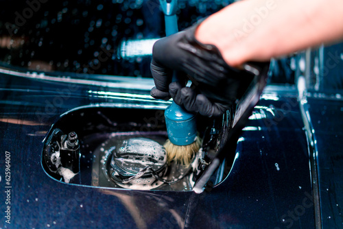 Close-up of a car wash employee washing the fuel cap space of a luxury blue car using a brush 