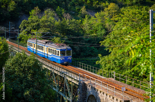 Historic electric train on famous steel bridge in Intragna in Centovalli valley. Famous narrow gauge railway line from Locarno to Domodossola in Italy in the Swiss Alps. Popular tourist train journey.