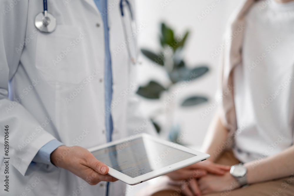 Doctor and patient discussing health exam results. Friendly physician reassuring a young woman by one hand while keeping tablet computer in another. Medicine concept Doctor and patient discussing health exam results. Friendly physician reassuring a young woman by one hand while keeping tablet computer in another. Medicine concept