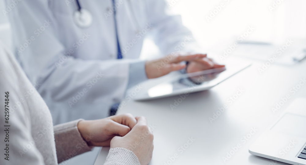 Doctor and patient sitting at the table in clinic while using tablet computer. The focus is on female patient's hands, close up. Medicine concept Doctor and patient sitting at the table in clinic while using tablet computer. The focus is on female patient's hands, close up. Medicine concept