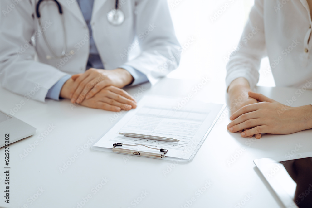 Doctor and patient discussing current health questions while sitting near of each other and using clipboard at the table in clinic, just hands closeup. Medicine concept Doctor and patient discussing current health questions while sitting near of each other and using clipboard at the table in clinic, just hands closeup. Medicine concept