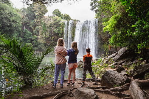 Three people, a mum and two children at an idyllic location looking at a waterfall, with their backs turned. This was taken at Whangarei Falls, New Zealand. photo