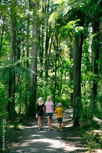A mum and two children are walking away from the camera in a beautiful forest trail in New Zealand.