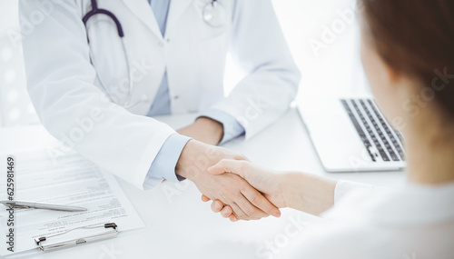 Doctor and patient shaking hands while sitting opposite of each other at the table in clinic  just hands close up. Medicine concept