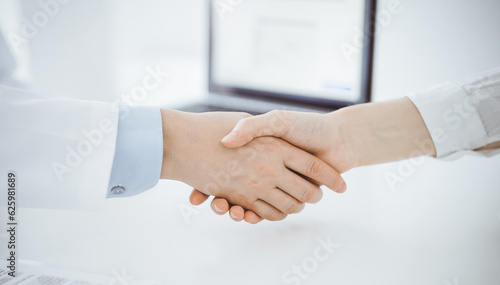 Doctor and patient shaking hands while sitting opposite of each other at the table in clinic, just hands close up. Medicine concept