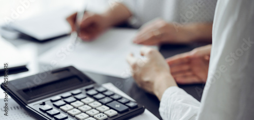 Woman accountant using a pen and laptop computer while counting and discussing taxes with a client  focus on the calculator. Business audit and finance concepts