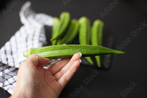 Hand holding okra or okro or lady's fingers warm season vegetable on the table. Ingredient of vegan diet. Good source of minerals, vitamins, antioxidants, and fiber.