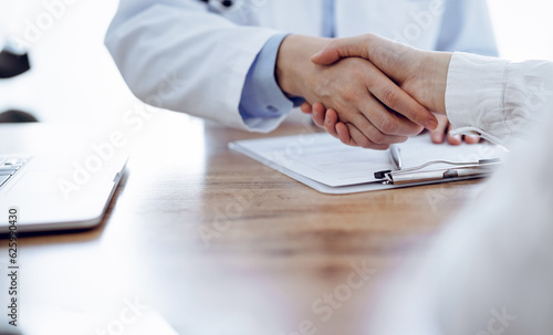 Doctor and patient shaking hands above the wooden table in clinic. Medicine concept
