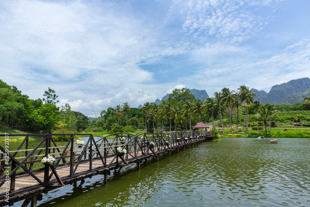 A wooden bridge crosses a pond behind which there is a forest and mountain garden. the sky is the background A wooden bridge crosses a pond behind which there is a forest and mountain garden. the sky is the background