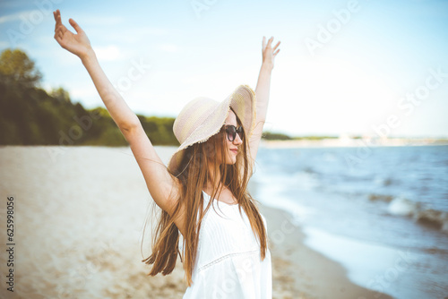 Wallpaper Mural Happy smiling woman in free happiness bliss on ocean beach standing with a hat, sunglasses, and rasing hands