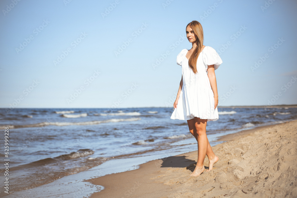 Happy smiling beautiful woman is walking on the ocean beach in a white summer dress Happy smiling beautiful woman is walking on the ocean beach in a white summer dress