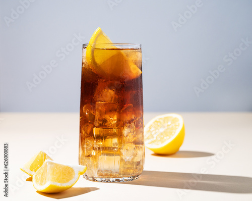 Iced tea with lemon and ice in a tall glass on a yellow background. The concept of a refreshing drink or lemonade on a hot summer day.