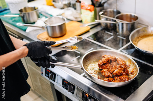 woman chef cooking chicken wings in a sauce in the kitchen