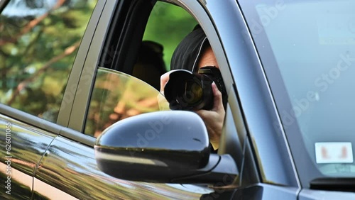 A private detective is sitting in the car, filming. The paparazzi sits in the car and photographs a famous person. Spy with a camera in the car.