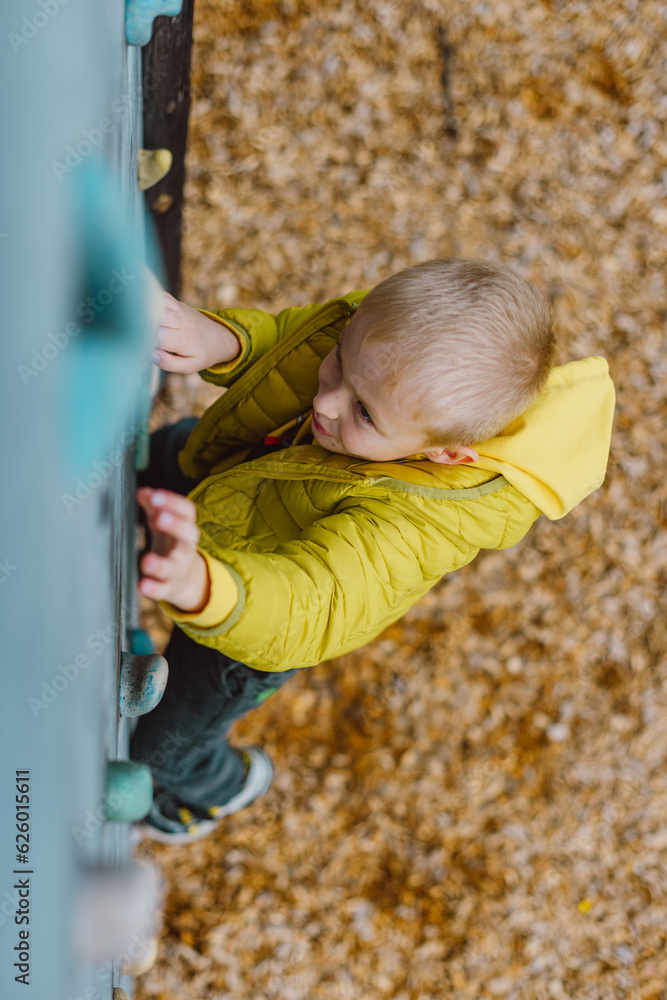 Boy At The Climbing Wall Without A Helmet, Danger At The Climbing Wall. Little Boy Climbing A Rock Wall Indoor Boy At The Climbing Wall Without A Helmet, Danger At The Climbing Wall. Little Boy Climbing A Rock Wall Indoor