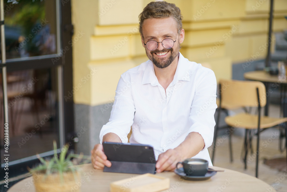 White-collar worker enjoying some time outdoors at cafe. He seated at table, dressed in crisp white shirt. With cup of coffee by side, engrossed in reading and accessing information on tablet PC. White-collar worker enjoying some time outdoors at cafe. He seated at table, dressed in crisp white shirt. With cup of coffee by side, engrossed in reading and accessing information on tablet PC.