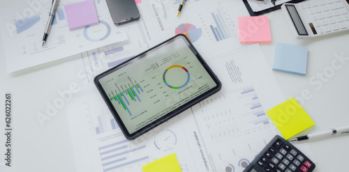 Business documents on office table with smart phone and calculator digital tablet and graph business with social network diagram and two colleagues discussing data working in office