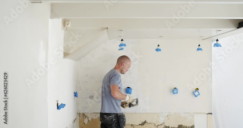 Man applying smoothing plaster on old wall. DIY renovation: Smoothing plaster on aged surface. applying plaster on old walls. How to renovate old walls with smoothing plaster