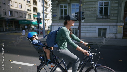 Cyclist mother riding bicycle in street with toddler in back seat © Marco