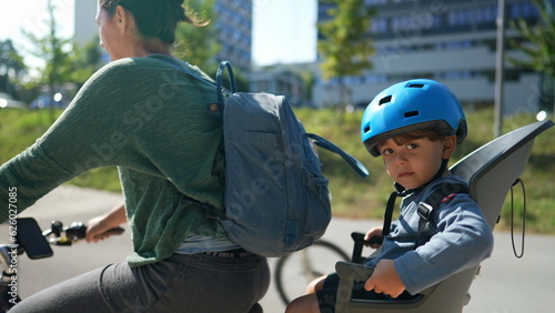 Mother riding bicycle with little boy sitting on back seat