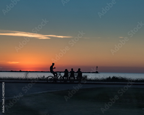 A group of four young people talking and enjoying a sunset over the port of Juan Lacaze
