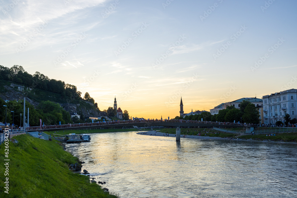 Salzach River runs through the city of Salzburg underneath a bridge at sunset