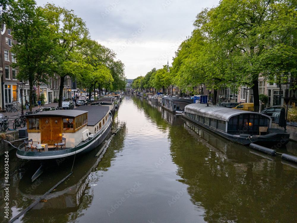 Houseboats line a tree-lined canal with calm water and reflections in the city of Amsterdam