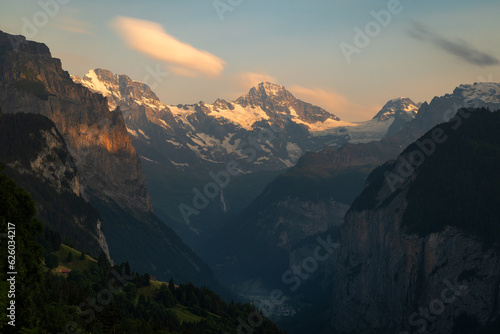Fading light on the snow covered mountains of the Swiss Alps create contrast on the grassy hillsides © Harrison