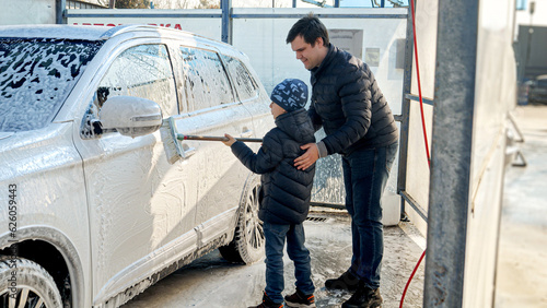 Young father teaching his little son wshing car at self service cash wash photo