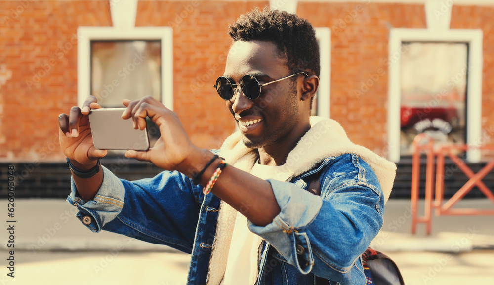 Portrait of happy smiling young african american man taking selfie with phone on city street - obrazy, fototapety, plakaty 
