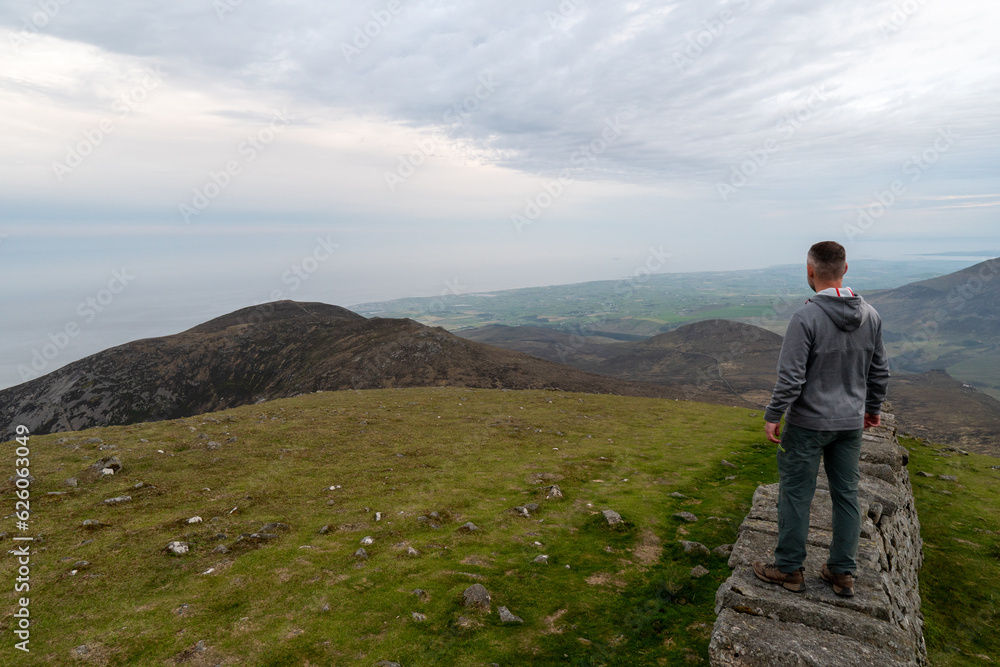 Panoramic view of typical Irish landscape, fields, sea in background. Picture taken from the top of the mountain. Hiker enjoing view after sunset Panoramic view of typical Irish landscape, fields, sea in background. Picture taken from the top of the mountain. Hiker enjoing view after sunset