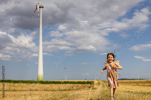 Curious happy girl is running near wind turbine on the field 