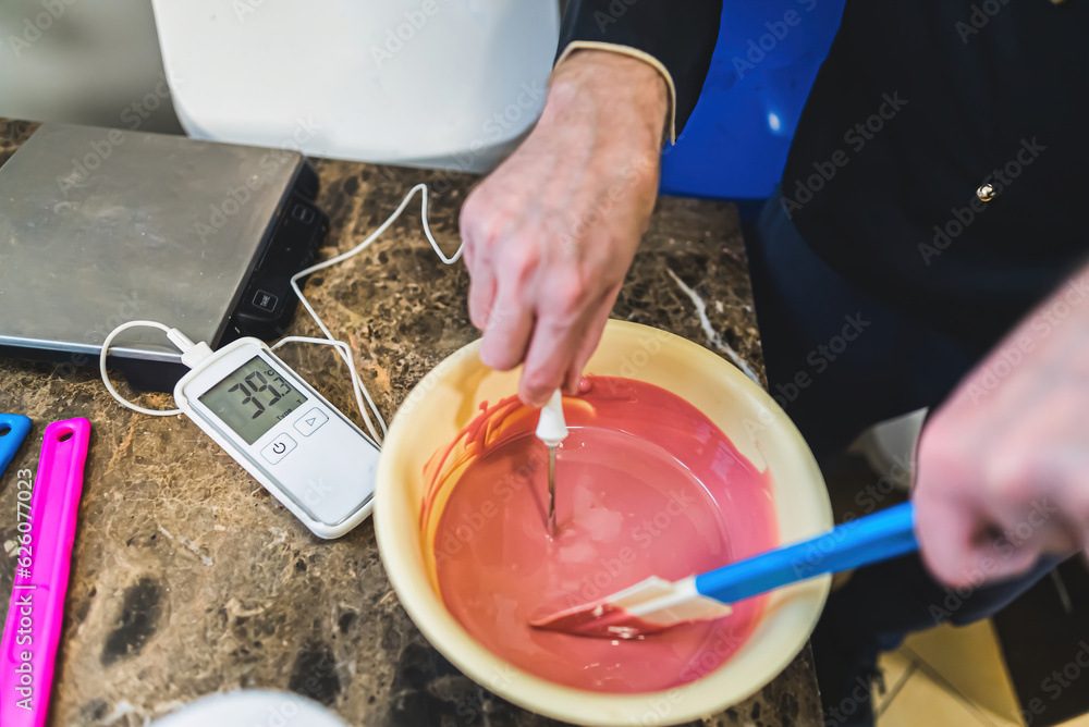 Top closeup shot of hands of chef measure temperature of melted ruby chocolate in bowl. Caucasian male professional preparing delicuoius ice cream. Cluttered ktchen background. High quality photo