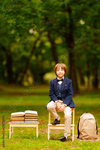 Cute schoolboy with books and backpack in the park, child studying outdoors. September 1. Last school bell. Back to school.High quality photo. Blurred background. 