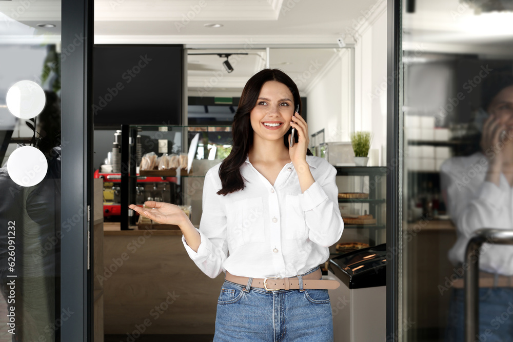 Business owner talking on smartphone at door of her cafe Business owner talking on smartphone at door of her cafe