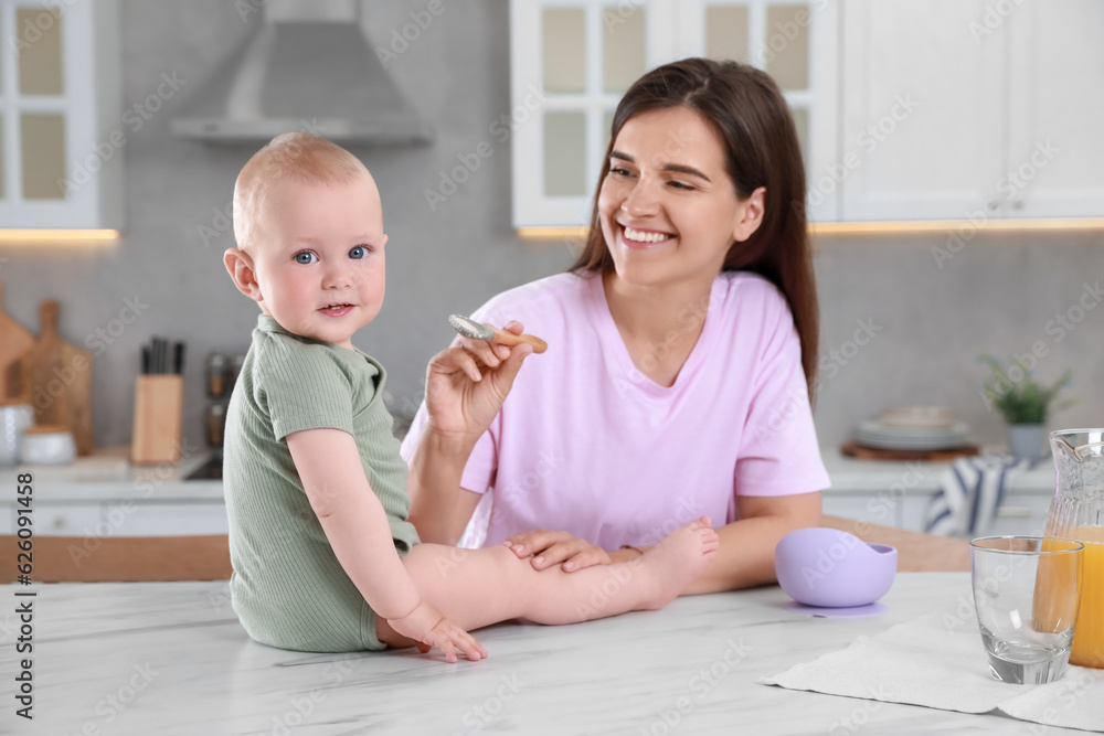 Happy young woman feeding her cute little baby at table in kitchen Happy young woman feeding her cute little baby at table in kitchen