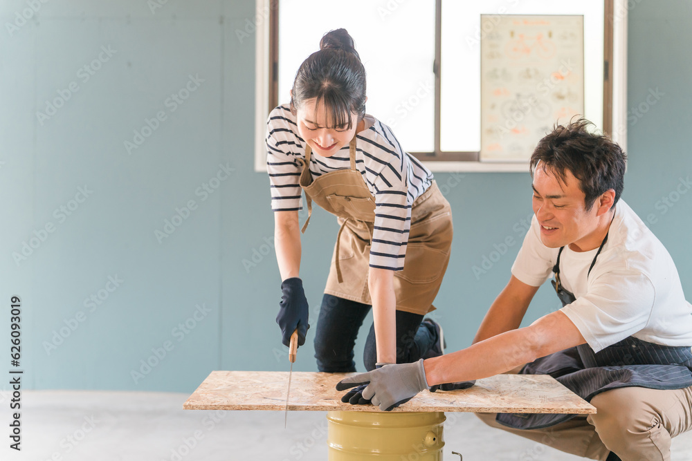 家の倉庫でノコギリで木を切るアジア人男女（DIY教室・ワークショップ・日曜大工・体験教室）
 - obrazy, fototapety, plakaty 