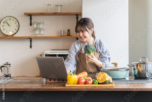 Tela 家のキッチンで自炊するためノートパソコンを使ってレシピや栄養素を検索する主婦のアジア人女性