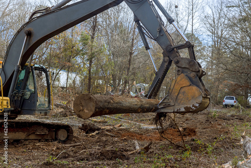 Worker is using an excavator to remove trees in forest a make way for house construction.