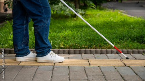 A blind woman walks outdoors using a cane along a tactile yellow tile.