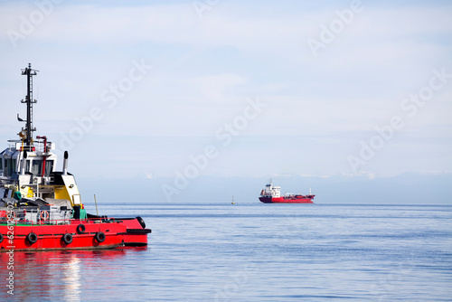 Bow of a red tugboat full of with cargo against the background of the sea with a ship in the distance