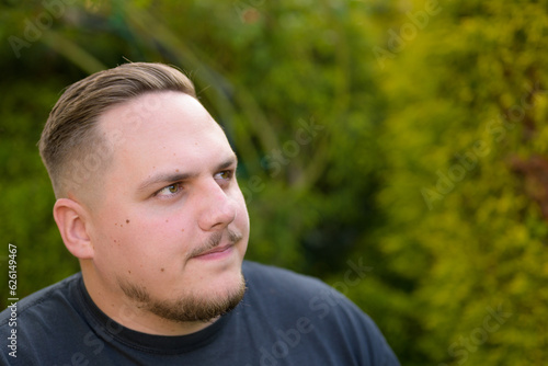 Portrait of a young man with a beard standing in the garden